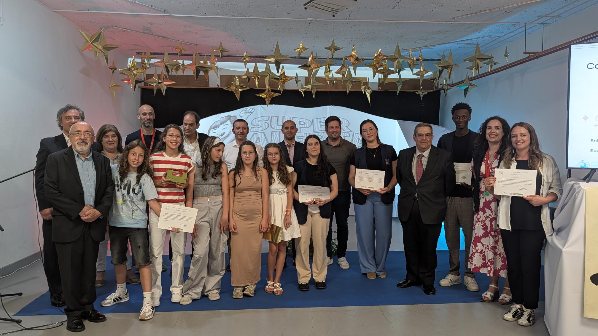  Grupo de pessoas alinhadas em palco durante uma cerimónia, algumas estão a segurar certificados. O cenário inclui uma estrutura com fundo onde se lê parcialmente “SUPER ALERTA”. No teto, estão suspensas várias estrelas douradas. Group of people lined up on stage during a ceremony, some are holding certificates. The scenario includes a structure with a background that reads partially “SUPER ALERTA”. On the ceiling are suspended several golden stars. 